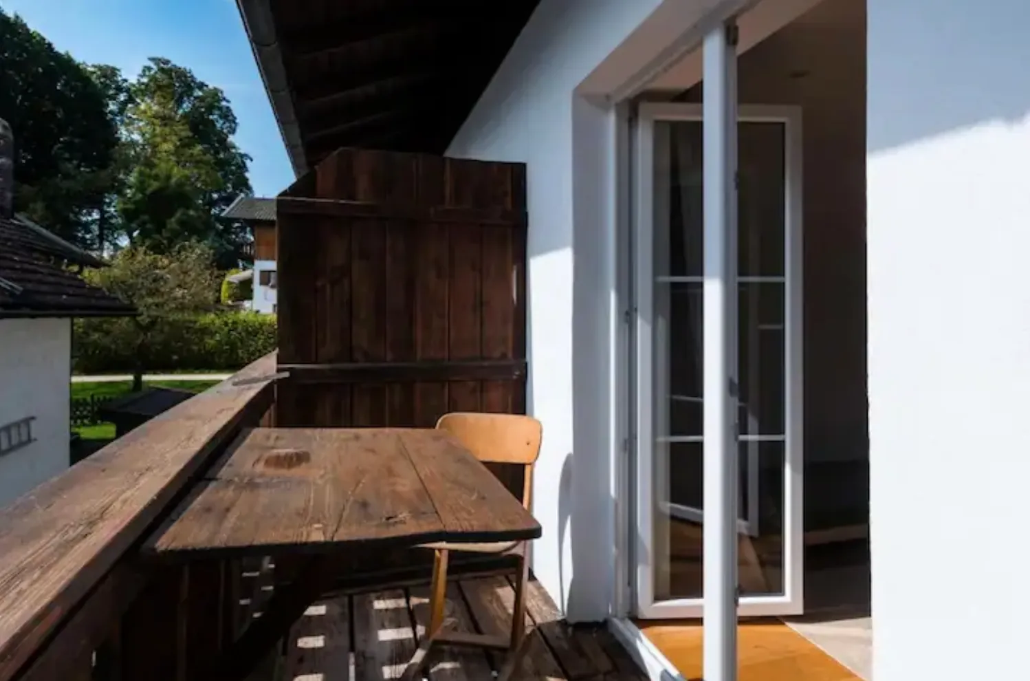 Sonniger Balkon mit Holztisch und Blick in den grünen Garten