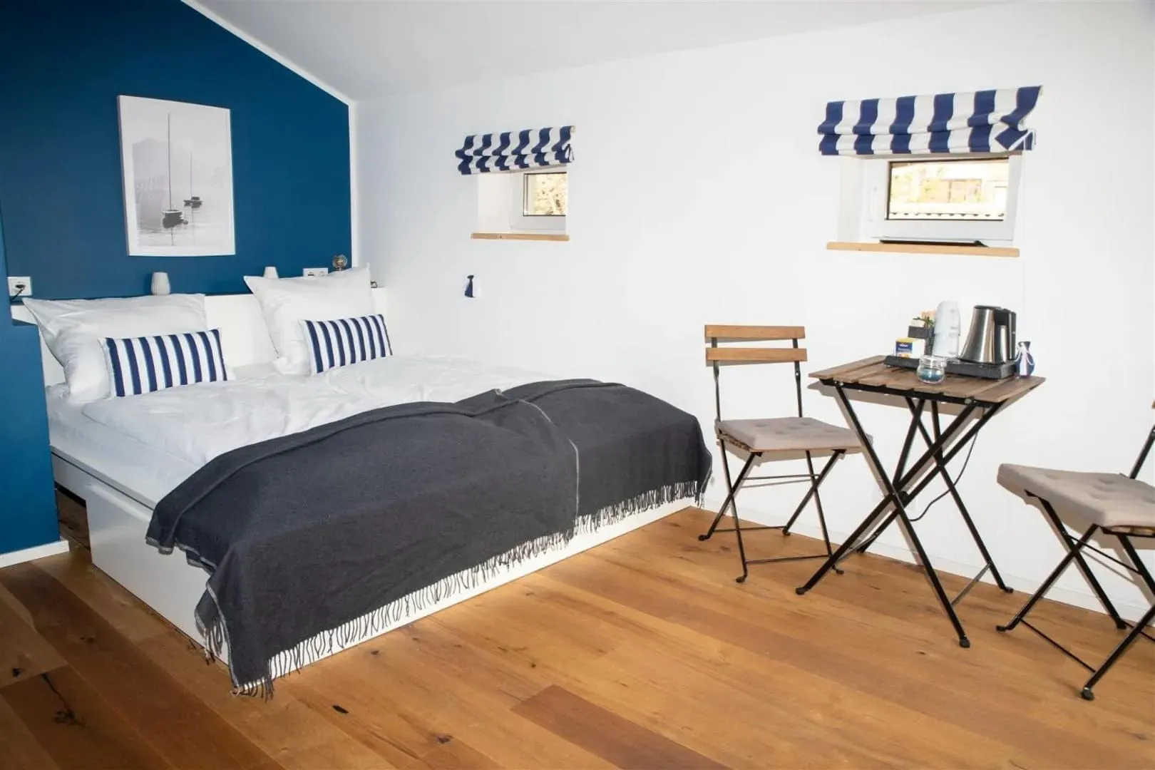 Helles Doppelzimmer mit blauer Wand, Doppelbett und kleinem Tisch am Fenster