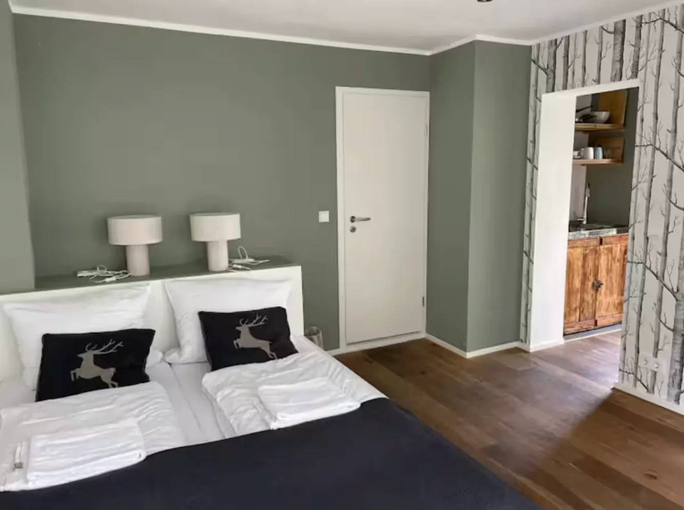 Zimmer mit salbeigrünen Wänden, Doppelbett und kleiner Küchenzeile